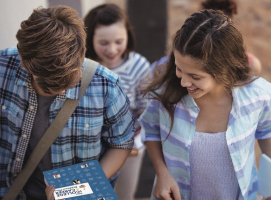 A group of people standing around each other holding IDEAS books